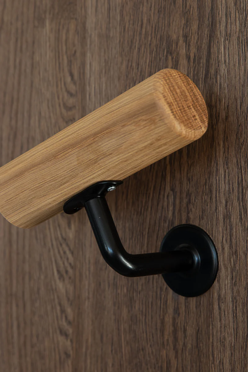 Close-up of an oak handrail mounted with a black wall bracket